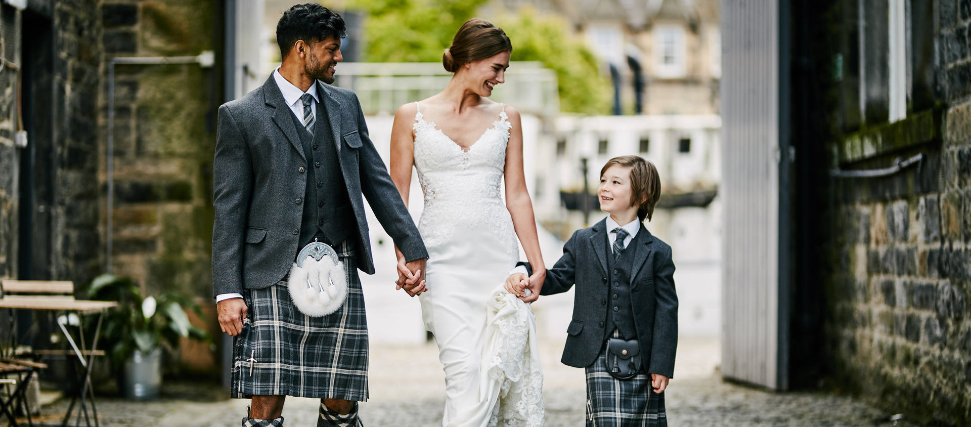 A groom, bride, and child dressed in full Highland hire outfits from Eight Yards, including kilt, jacket, and accessories.